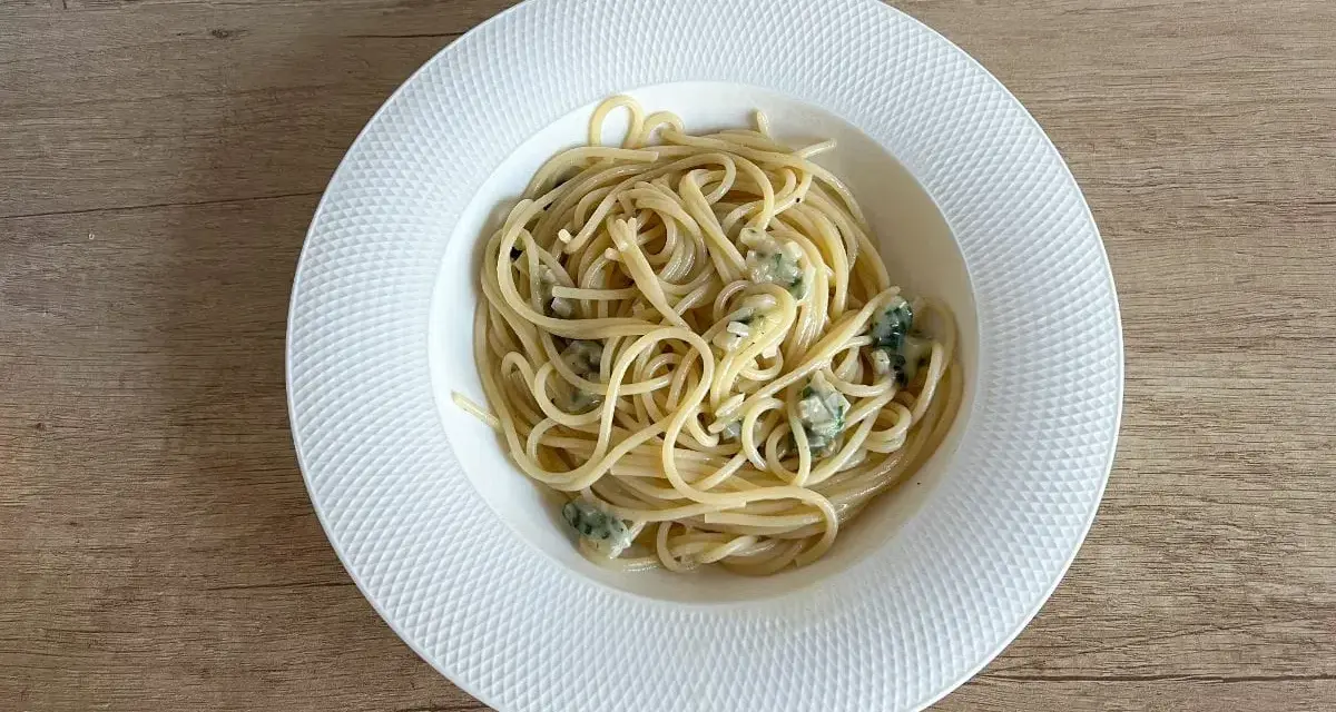 Pyszne spaghetti aglio olio z kawałkami sera pleśniowego na białym talerzu.