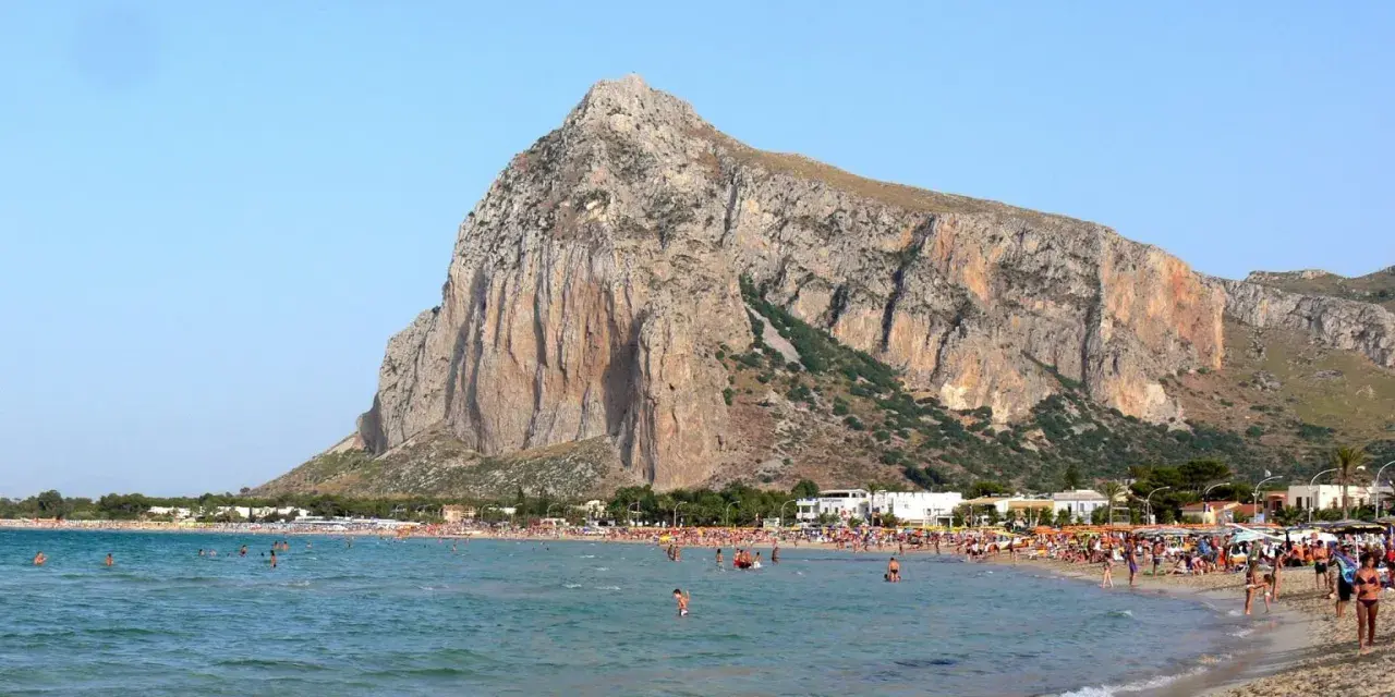 Słoneczna plaża w San Vito Lo Capo, z turkusową wodą i majestatyczną górą w tle. Tłumy ludzi cieszą się wakacjami.