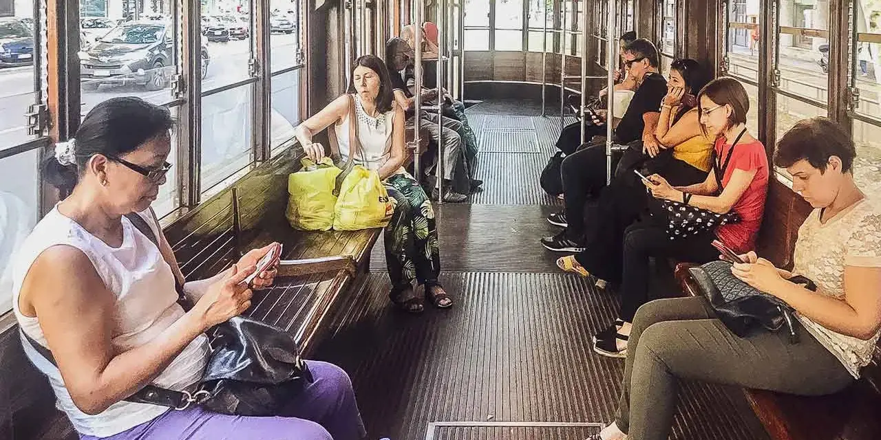 Wnętrze tramwaju w Mediolanie. Pasażerowie korzystają z mediolańskiej komunikacji miejskiej, przeglądając telefony.