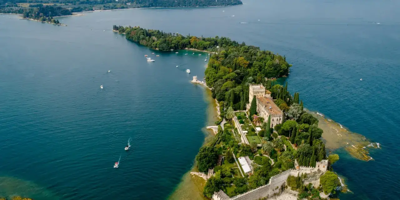 Malowniczy widok na Isola del Garda z pałacem i ogrodami, otoczony turkusową wodą jeziora.