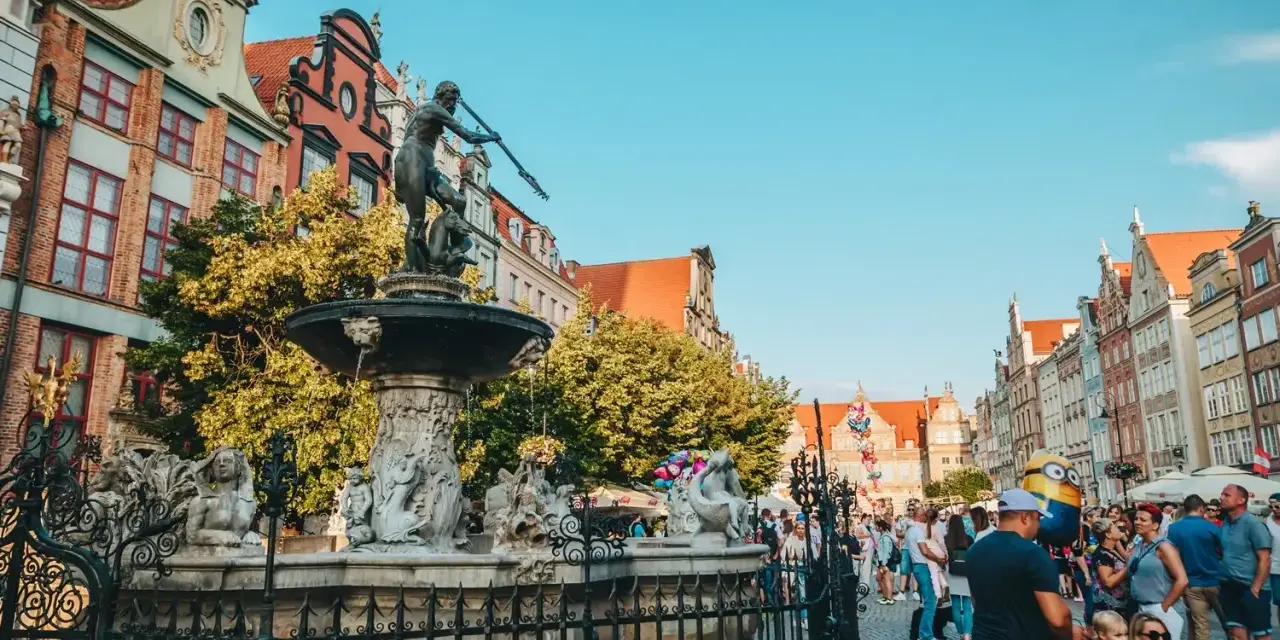 Fontanna Neptuna na tle kamienic i tłumu ludzi w Gdańsku.