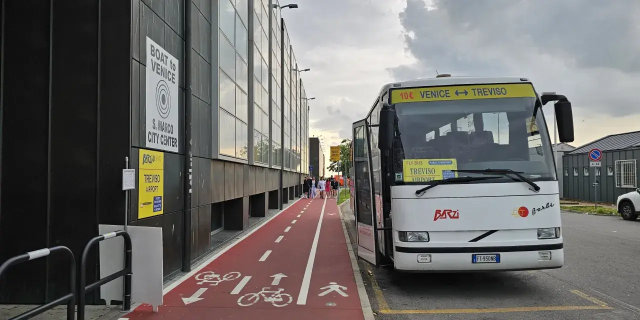 Autobus z napisem "Venice Treviso" czeka na pasażerów przy lotnisku. Obok czerwona ścieżka rowerowa i piesza.