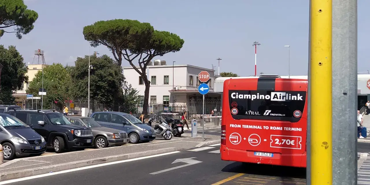 Czerwony autobus Ciampino Airlink na tle parkingu i budynków.