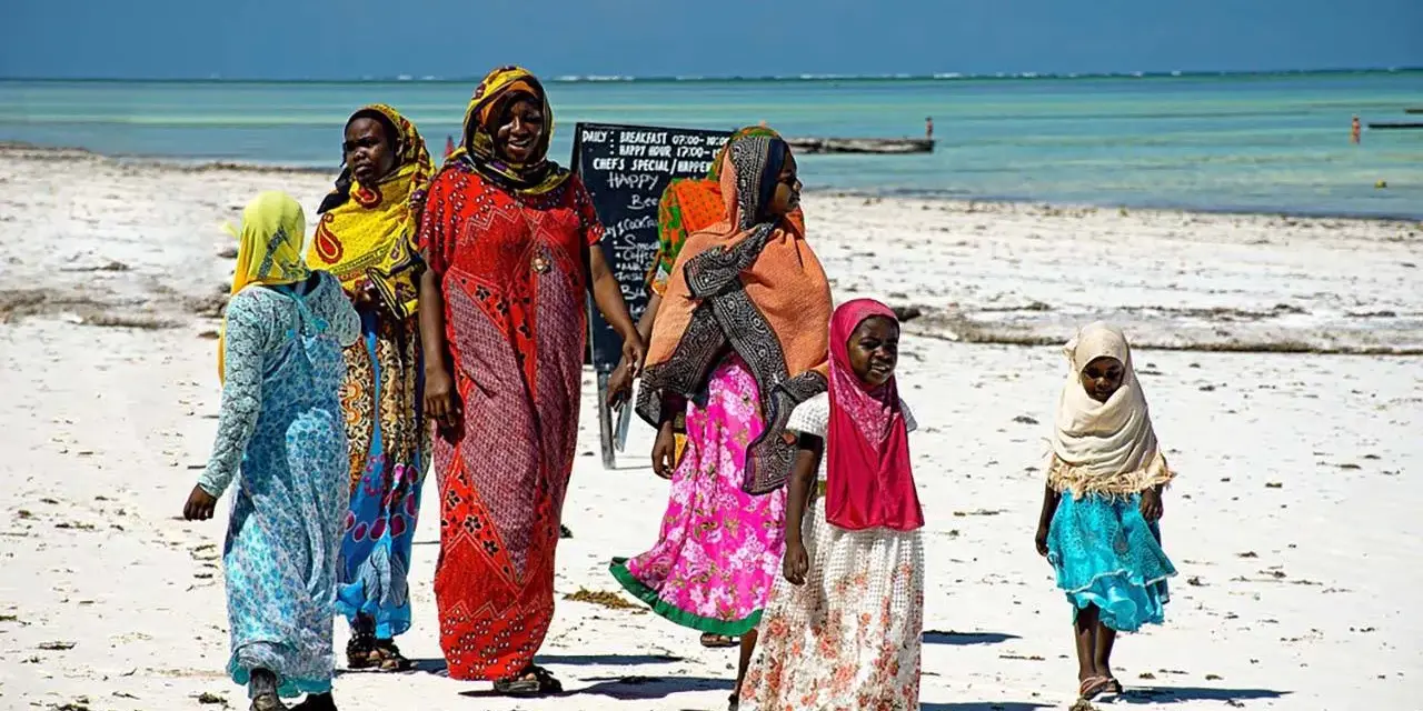 Kobiety w kolorowych strojach spacerują po plaży Zanzibaru. Warto wiedzieć, że to miejsce oferuje piękne widoki i lokalną kulturę.