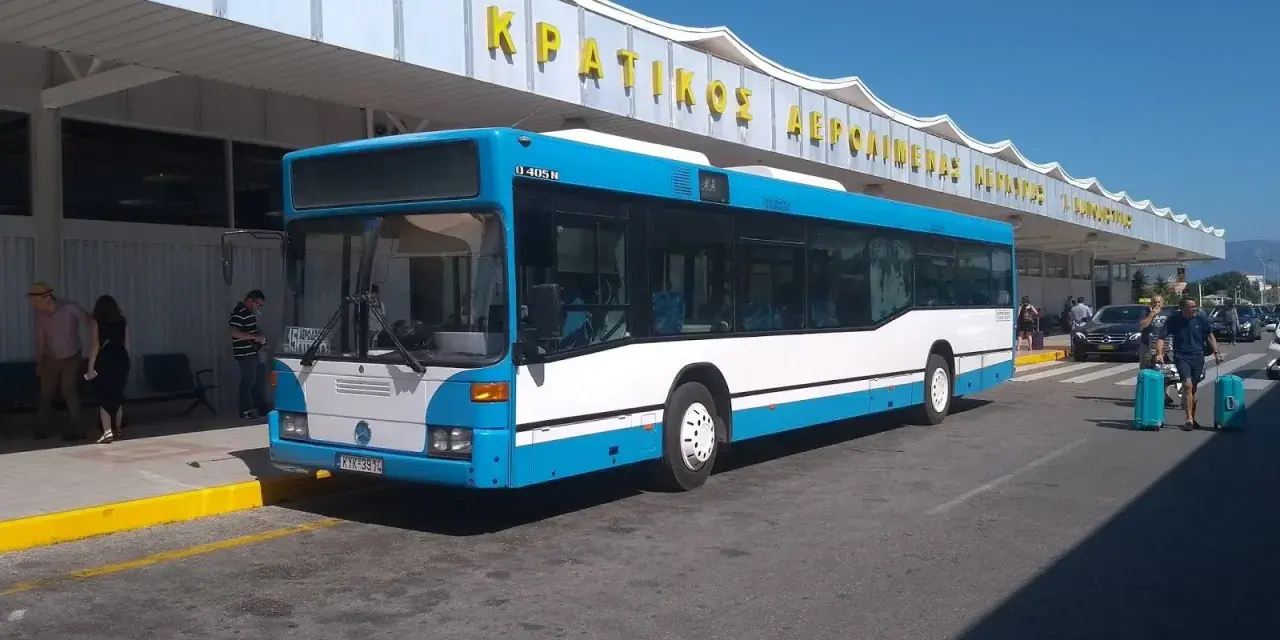 Niebiesko-biały autobus na tle budynku lotniska z żółtym napisem.