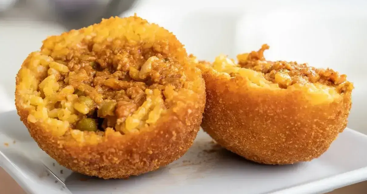 Arancini co to? Chrupiące kulki ryżowe z mięsnym farszem i groszkiem, przekrojone na pół, prezentują swoje bogate wnętrze.
