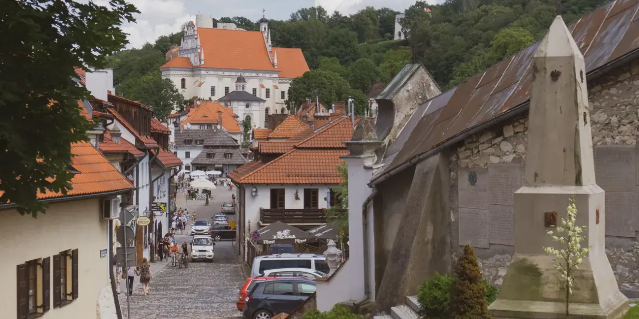 Widok na urokliwą, brukowaną uliczkę Kazimierza Dolnego z zabytkową architekturą i kościołem w tle.