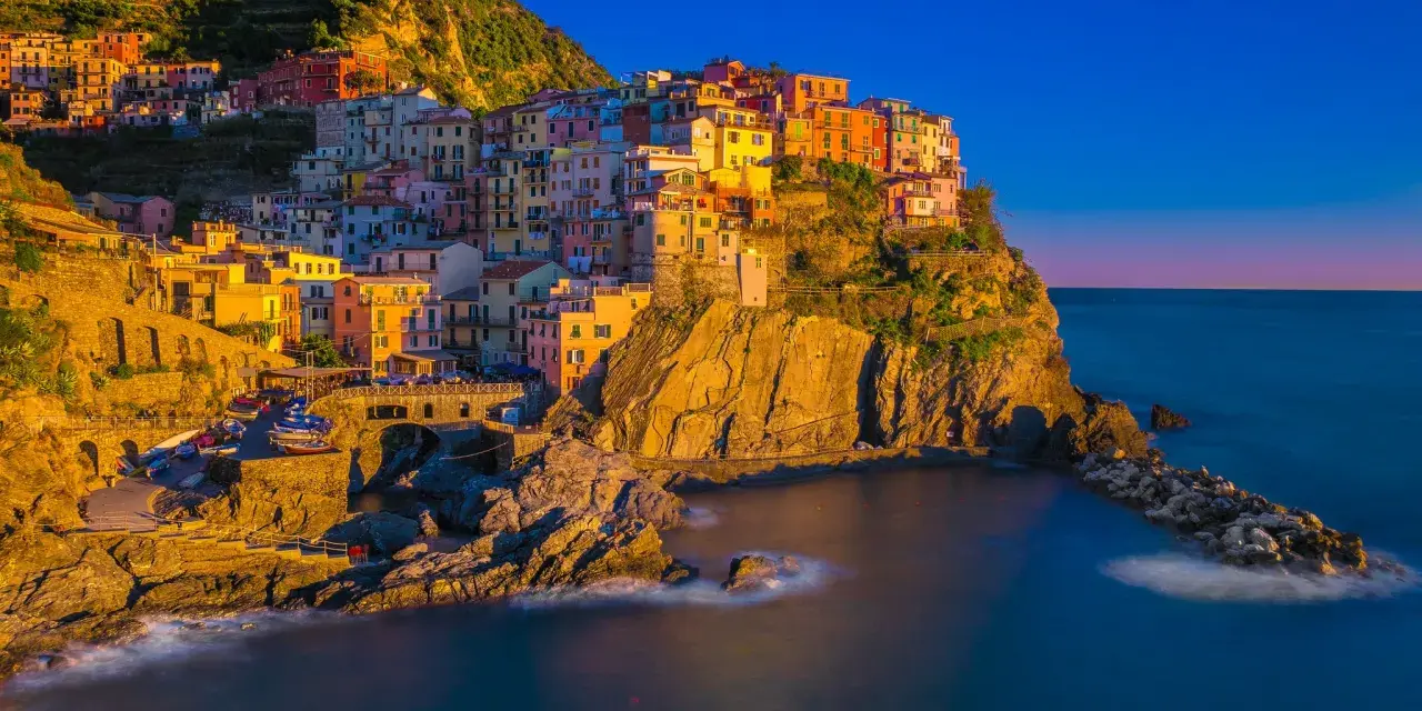 Kolorowe domy Cinque Terre w **Włoszech we wrześniu**, oświetlone złotym słońcem, schodzą ku morzu.