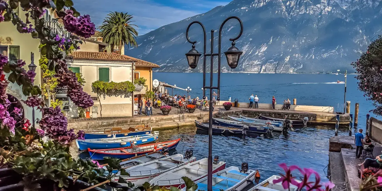 Malowniczy port z łodziami, budynkami i górami w tle nad Jeziorem Garda.