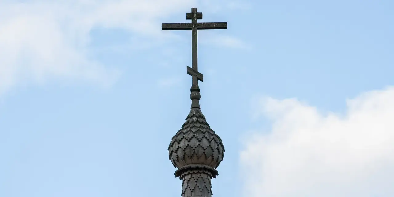Drewniany krzyż prawosławny na tle błękitnego nieba z chmurami.