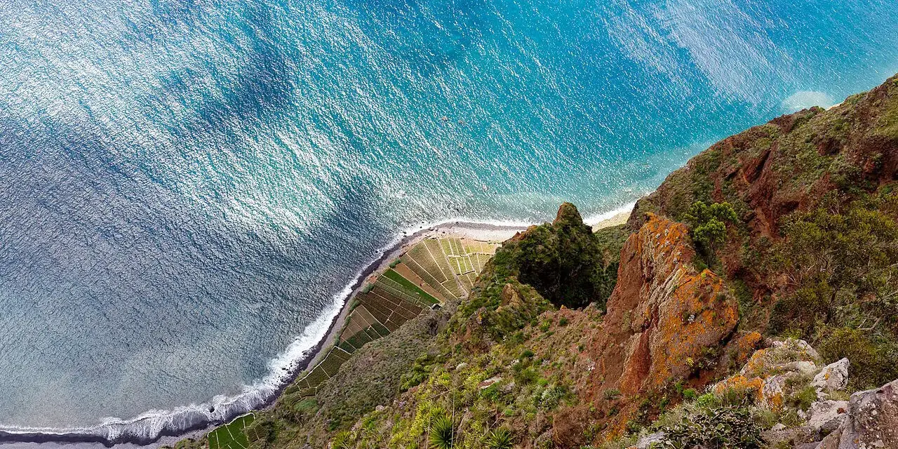 Widok z góry na klif Madery, pola uprawne i ocean.