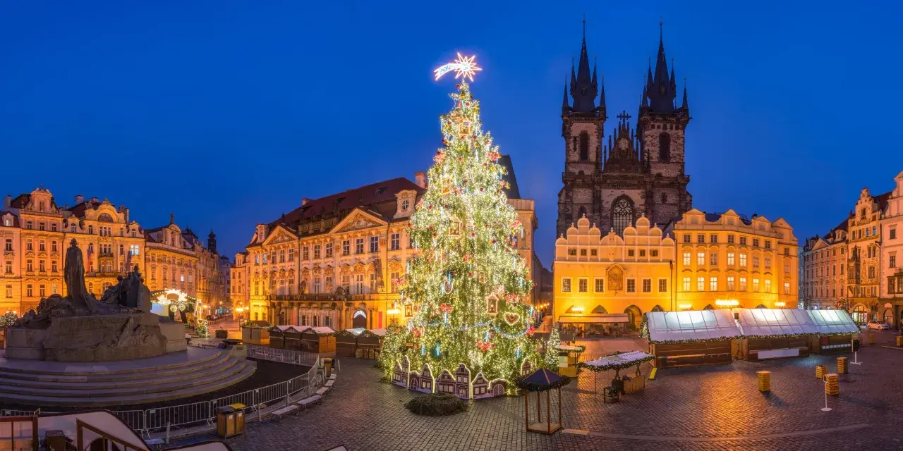Jarmark bożonarodzeniowy w Pradze. Ogromna, oświetlona choinka na Rynku Staromiejskim, w tle gotycka architektura i zabytkowe kamienice.