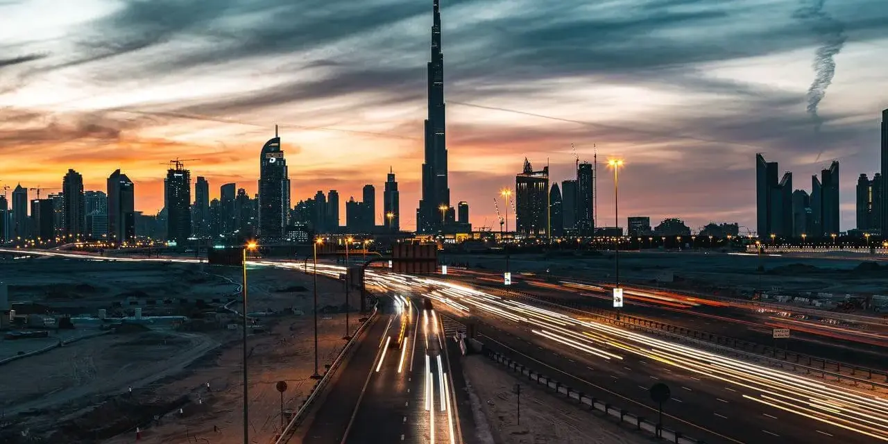 Wieczorny widok na Dubaj z Burj Khalifa, gdzie światła samochodów tworzą smugi na autostradzie. Ciekawostki o tym drapaczu chmur mogą dotyczyć jego wysokości i budowy.