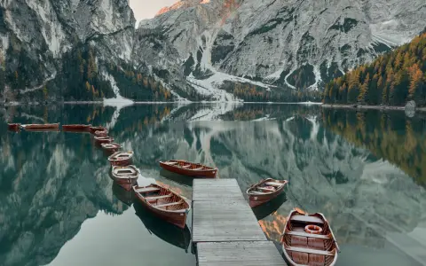 Drewniane łodzie przy drewnianym pomoście na spokojnym Lago di Braies, odbijające się w tafli wody, z majestatycznymi górami w tle.