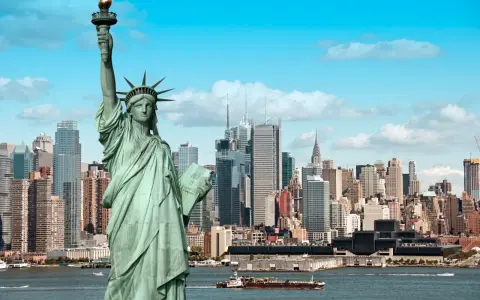 Statua Wolności wita podczas podróży do USA. W tle panorama Nowego Jorku z drapaczami chmur i statkami na rzece.