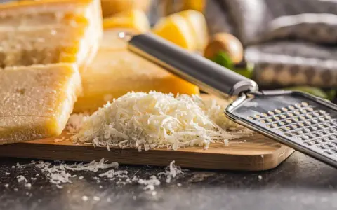 Stos tartego parmezanu, znanego jako parmigiano reggiano, obok bloków sera i tarki.