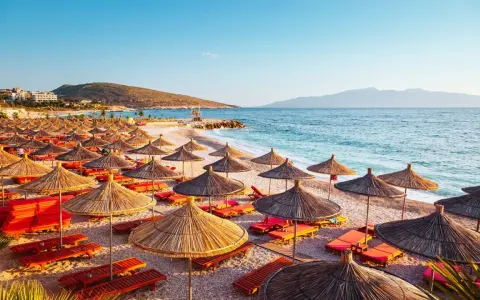 Albania, lipiec: słoneczna plaża z rzędami parasoli i leżaków, turkusowe morze i góry w tle. Idealna pogoda na wakacje.