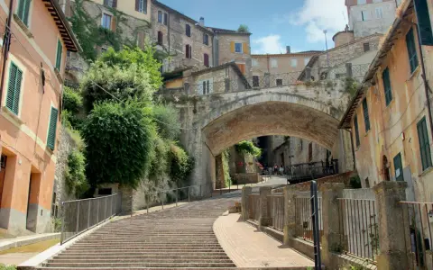 Perugia co zobaczyć: malownicze schody prowadzące pod zabytkowy most, otoczone kamiennymi domami i zielenią.
