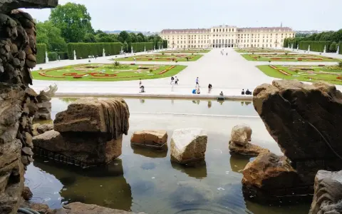 Wiedeń ogrody Sisi: malowniczy widok na pałac Schönbrunn i jego kwieciste tarasy, z kamienną fontanną w pierwszym planie.