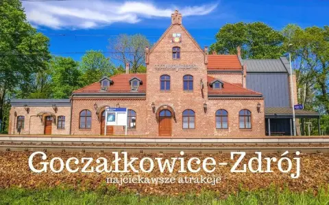 Ceglana stacja kolejowa Goczałkowice-Zdrój z czerwonym dachem i zielonymi drzewami w tle.