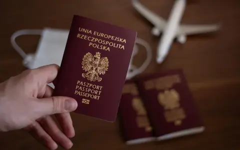 Dłoń trzyma polski paszport. Obok leżą kolejne dokumenty, maseczka i model samolotu. Zastanawiasz się, ile trwa wyrobienie paszportu?