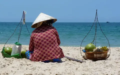 Sprzedawczyni kokosów na plaży w Mui Ne, Wietnam. W tle błękitne morze i niebo.