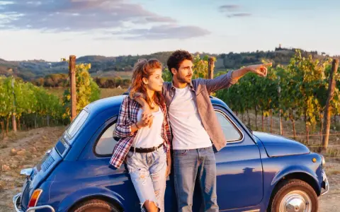 Para młoda przy niebieskim Fiat 500, podróżując samochodem do Włoch, podziwia toskańskie wzgórza.
