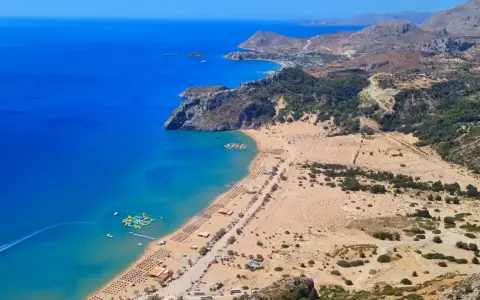 Widok z lotu ptaka na piaszczystą plażę z leżakami, turkusowe morze i górzysty krajobraz Rodos.