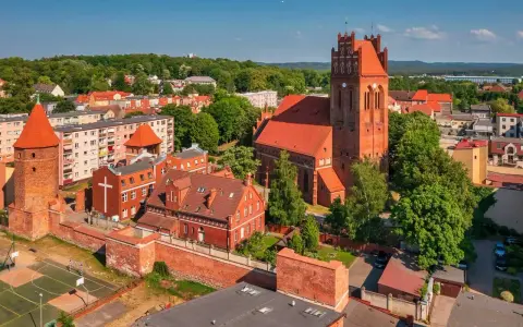 Zamek krzyżacki w Lęborku, z charakterystyczną wieżą i ceglaną architekturą, otoczony zielenią i zabudowaniami miejskimi.