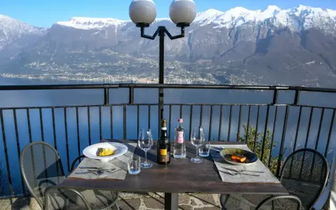 Stół z winem i jedzeniem na tarasie z widokiem na jezioro i ośnieżone góry. Idealne miejsce na romantyczną kolację z widokiem, prawdziwa "terrazza del brivido".