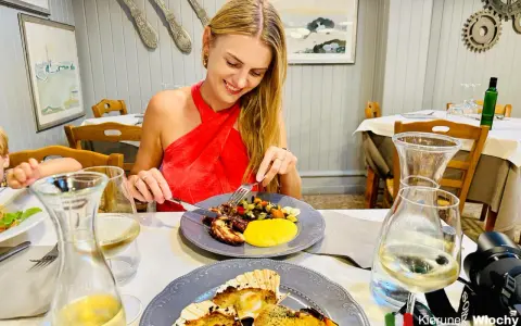 Szukasz miejsca, gdzie zjeść w Wenecji? Uśmiechnięta kobieta delektuje się daniem z ośmiornicy i warzywami w urokliwej restauracji.