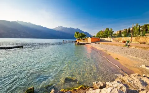 Słoneczna plaża nad jeziorem Garda z kamienistym brzegiem i łagodnymi falami.