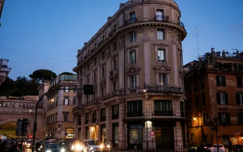 Wieczorna ulica w Rzymie z zabytkowymi budynkami i ruchem ulicznym.