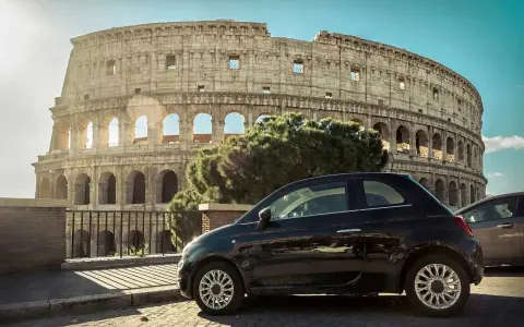 Czarny Fiat 500 pod Koloseum w Rzymie. Zastanawiasz się, ile się jedzie z Polski do Włoch samochodem?