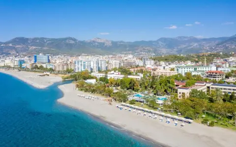 Widok z lotu ptaka na kurort nad morzem w Turcji z plażą, hotelami i górami w tle.