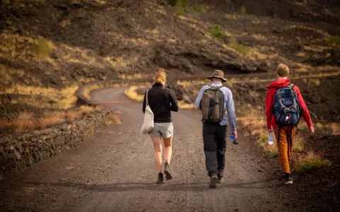 Trzy osoby wędrują po wulkanicznym krajobrazie Sycylii. Styczeń na wyspie oferuje przyjemną temperaturę do trekkingu.