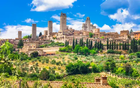 Widok na średniowieczne wieże i zabudowania San Gimignano w Toskanii, otoczone zielenią i winnicami.