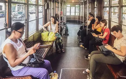 Wnętrze tramwaju w Mediolanie. Pasażerowie korzystają z mediolańskiej komunikacji miejskiej, przeglądając telefony.