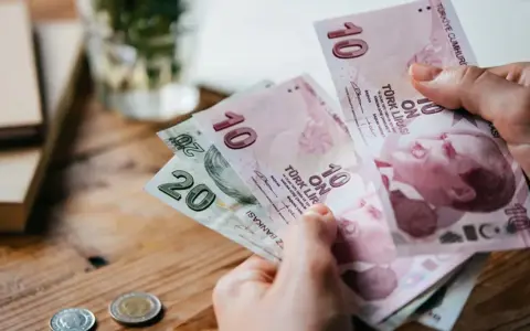 Ręka trzyma banknoty 10 i 20 lir tureckich. To pokazuje, czym płacić w Turcji.