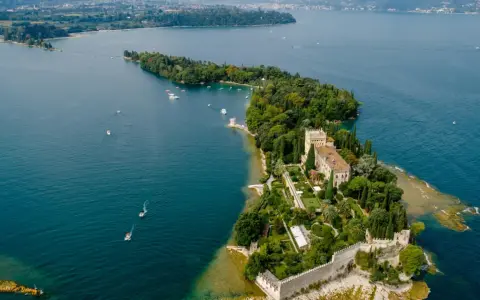 Malowniczy widok na Isola del Garda z pałacem i ogrodami, otoczony turkusową wodą jeziora.
