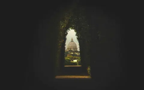 Widok na kopułę Bazyliki św. Piotra przez zielony tunel w ogrodach pomarańczowych Rzym.