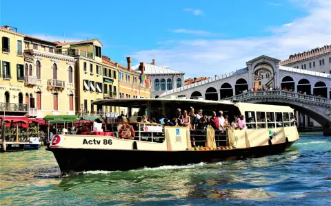 Pasażerowie płyną tramwajem wodnym w Wenecji, mijając zabytkowe budynki i Most Rialto.