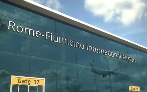 Lotnisko Rzym Fiumicino. Jak dojechać do centrum? Widok na nowoczesny budynek lotniska z napisem "Rome-Fiumicino International Airport" i odbijającym się samolotem.