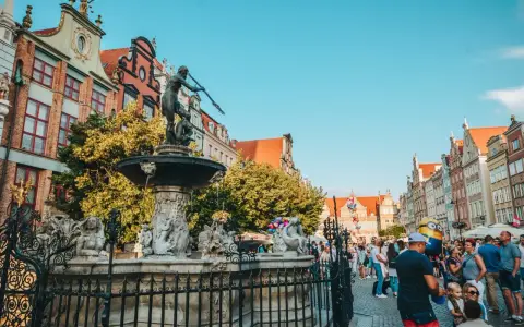Fontanna Neptuna na tle kamienic i tłumu ludzi w Gdańsku.