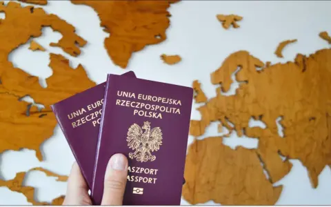 Dwa polskie paszporty w dłoni na tle drewnianej mapy świata. Planujesz podróż? Dowiedz się, jak wyrobić paszport.