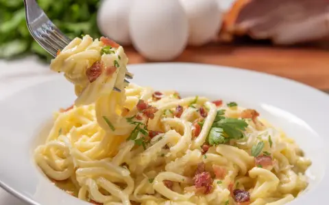 Pyszne spaghetti carbonara przepis na talerzu, z widocznymi jajkami i boczkiem w tle. Idealne danie dla miłośników włoskiej kuchni.