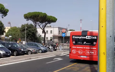 Czerwony autobus Ciampino Airlink na tle parkingu i budynków.