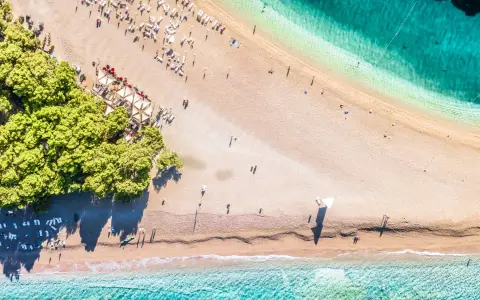 Chorwacja plaże piaszczyste, z turkusową wodą i zielonymi drzewami. Leżaki i parasole czekają na plażowiczów.