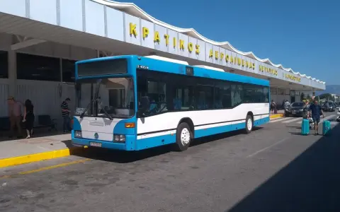 Niebiesko-biały autobus na tle budynku lotniska z żółtym napisem.