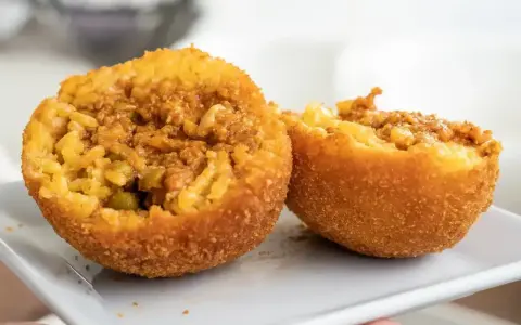 Arancini co to? Chrupiące kulki ryżowe z mięsnym farszem i groszkiem, przekrojone na pół, prezentują swoje bogate wnętrze.